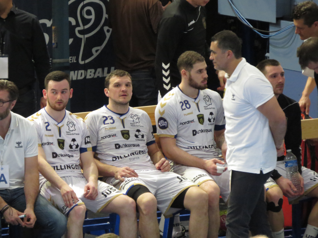 Eine Gruppe von Männern sitzt auf einer Bank, einige halten Flaschen, im Hintergrund ist eine Fahne mit der Aufschrift "Nordkraque vs Bordeaux."