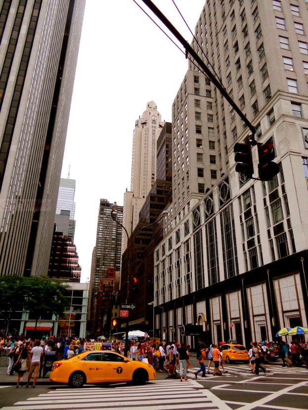 Eine Stadtstraßenszene mit Gebäuden, Ampeln, Fenstern, wenigen Fußgängern, Autos und Himmel.