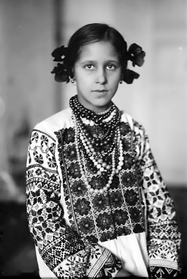 Ein junges Mädchen in einem geschmückten Kleid, eingefangen in einem unscharfen, schwarz-weißen Foto mit nostalgischer Atmosphäre.