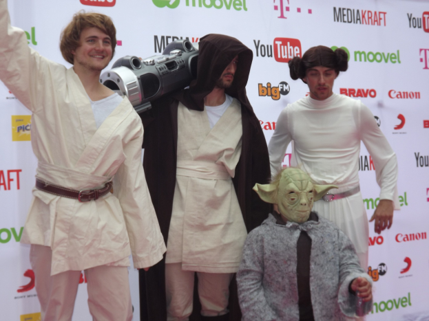 Eine Gruppe von Menschen in Star-Wars-Kostümen posiert auf einem roten Teppich mit einem Banner im Hintergrund.