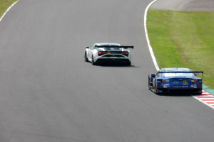 Zwei Sportwagen auf einer Rennstrecke mit Gras auf beiden Seiten.