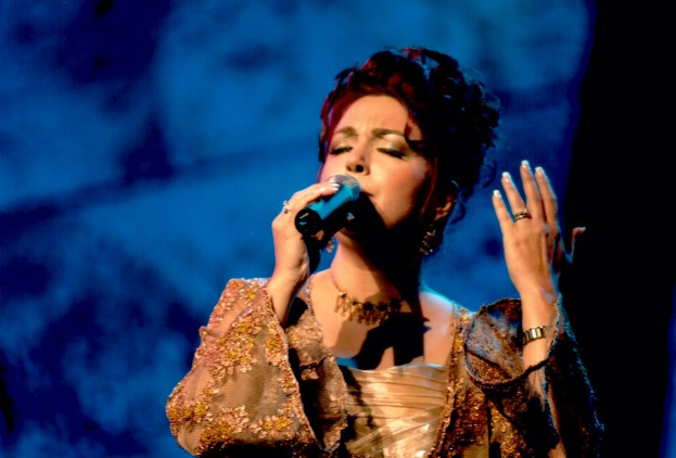 Frau in goldenem Kleid singend ins Mikrofon auf der Bühne beim Eurovision Song Contest mit blau-schwarzem Hintergrund.