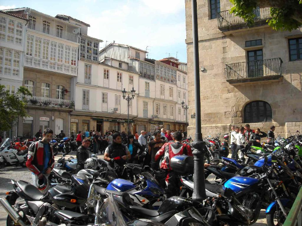 Ein cremefarbenes Gebäude mit zahlreichen Fenstern, angrenzend an ein Backsteingebäude mit einer Metallrahmen-Balkon, mit mehreren geparkten Fahrrädern und Menschen, die vor dem Gebäude plaudern.