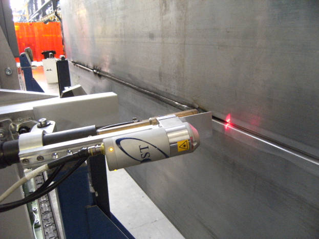 Eine Laser-Schneidmaschine in einer Fabrik strahlt helles Licht aus, mit einer Wand auf der rechten Seite und Hintergrundgegenständen.