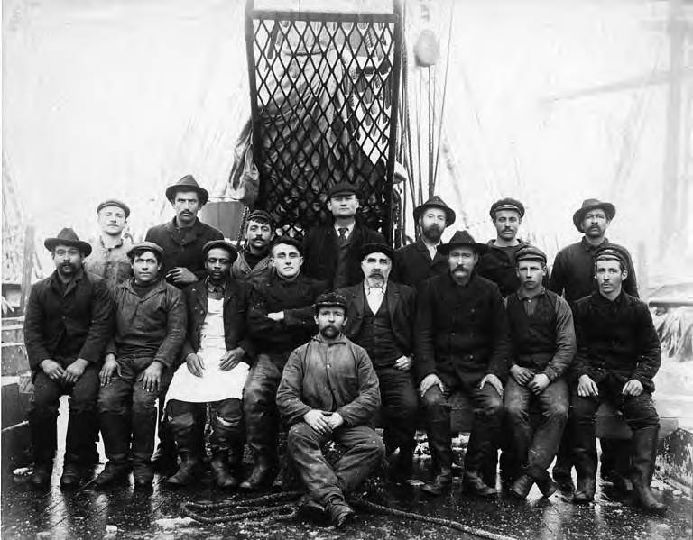 Schwarz-weißes Foto von Männern in Hüten auf einem Boot mit einem Netz und Seilen im Hintergrund.