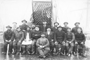 Schwarz-weißes Foto von Männern in Hüten auf einem Boot mit einem Netz und Seilen im Hintergrund.