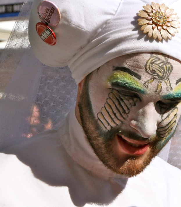 Ein Mann mit Gesichtsbemalung und einer Cap mit Text, der vor einem Stoffhintergrund steht.