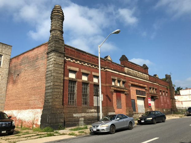 Alter Backsteinbau mit seitlichem Schornstein, identifiziert als ehemalige St. Louis Feuerwache, umgeben von Straßenlaternen, Fahrzeugen, Schildern, Bäumen und einem bewölkten Himmel.