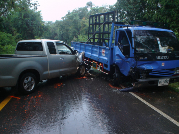 Ein schwerbeschädigter Lkw mit eingedrückter Front und verbeulter Karosserie liegt am Straßenrand, umgeben von Bäumen unter einem klaren blauen Himmel.