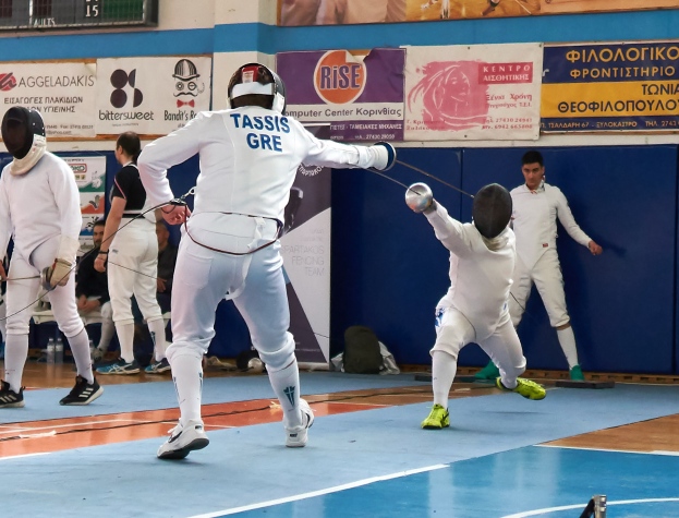 Eine Gruppe von Menschen beim Fechten in einer Turnhalle mit Bannern an der Wand und einer Anzeigetafel oben, alle tragen Helme und halten Schwerter.
