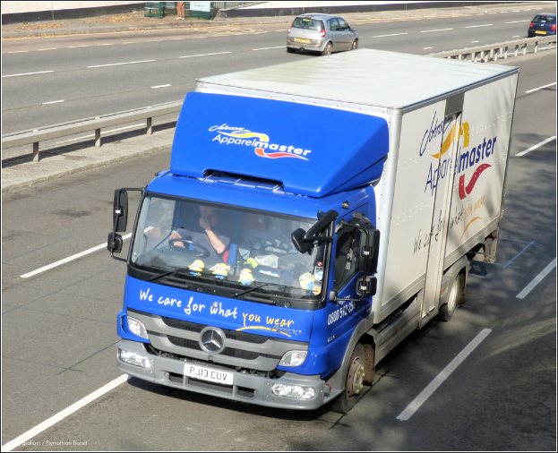 Eine Straße mit einigen Fahrzeugen, einer zentralen Leitplanke und einer Metallkonstruktion oben.