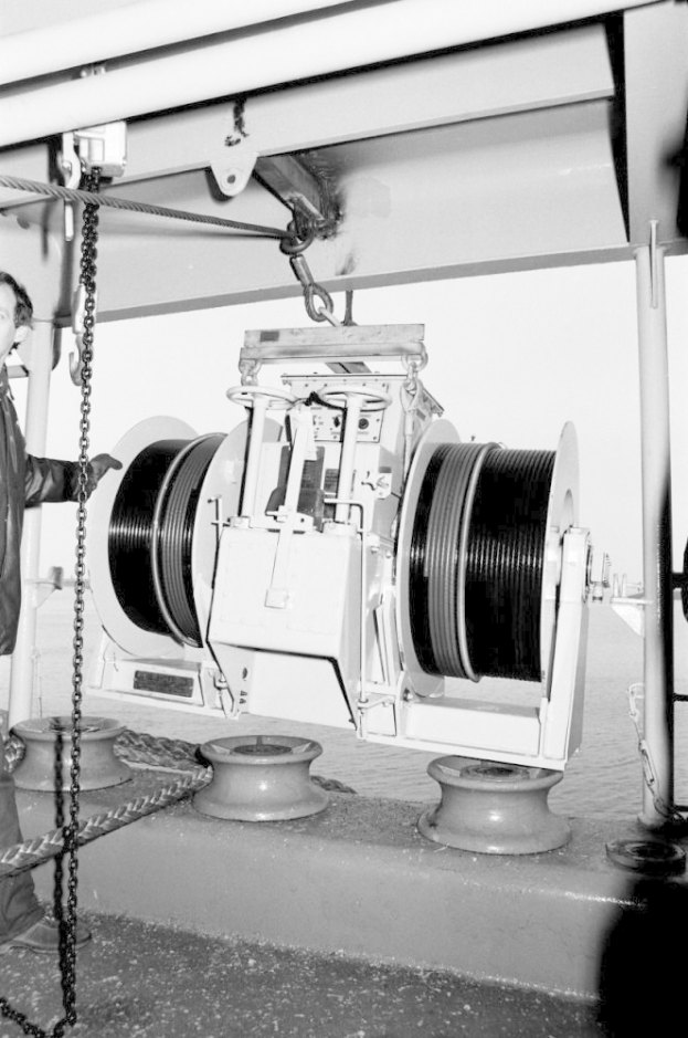 Ein Mann in Schuhen steht neben einer großen Maschine mit einer Kette in einem zeitlosen Schwarz-Weiß-Bild.