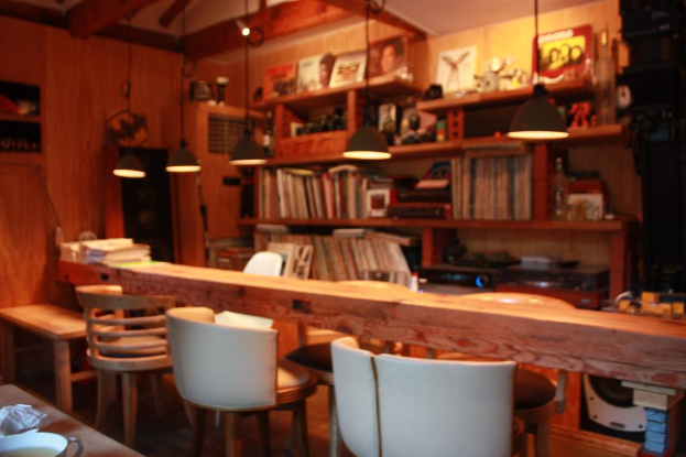 Ein Bücherregal mit Lampen und einer Wand im Hintergrund, mit drei Stühlen und einem Tisch auf der linken Seite des Raums.