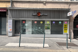 Ein Gebäude mit einem zerbrochenen Glasfenster an der Seite, umgeben von Pfosten und einer Straße, mit Fenstern, Rollläden und Brettern mit der Aufschrift "Departamento Cash Express".