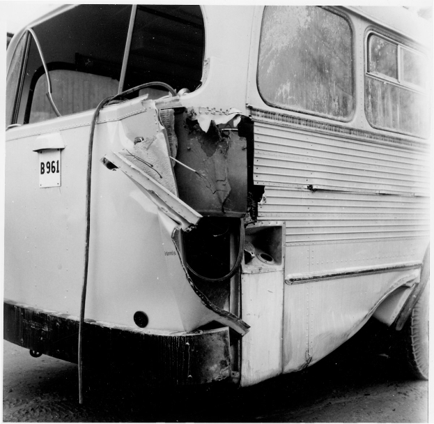Schwarz-weiß-Foto eines Busses mit schwerer Frontschaden nach einer Kollision mit einem Auto, das auf der Straße positioniert ist.