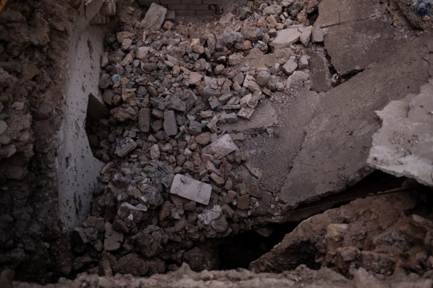 Einsturzendes Gebäude mit einem großen Loch im Boden, umgeben von Trömmern und einem sichtbaren Rohr auf der linken Seite, das Erdbebenschäden anzeigt.