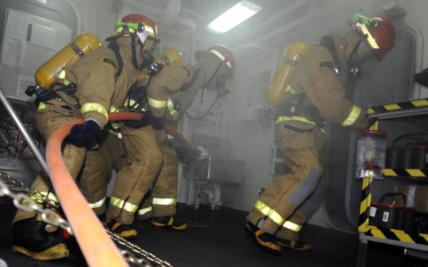 Feuerwehrleute in Schutzausrüstung arbeiten an einem Feuerwehren mit Ausrückungsgestellen und Hintergrundinfrastruktur.