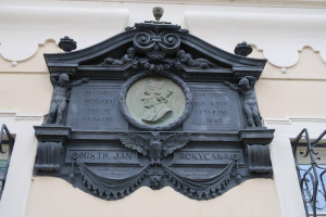 Metallplatte mit einer Skulptur und Text, an der Außenwand eines Gebäudes zwischen zwei Fenstern in Prag, Tschechische Republik angebracht.