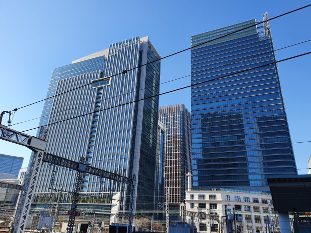 Stadtstraße mit hohen Gebäuden, Stromleitungen, Strommasten, Straßenlaternen, Verkehrszeichen, Bäumen und einem klaren blauen Himmel.