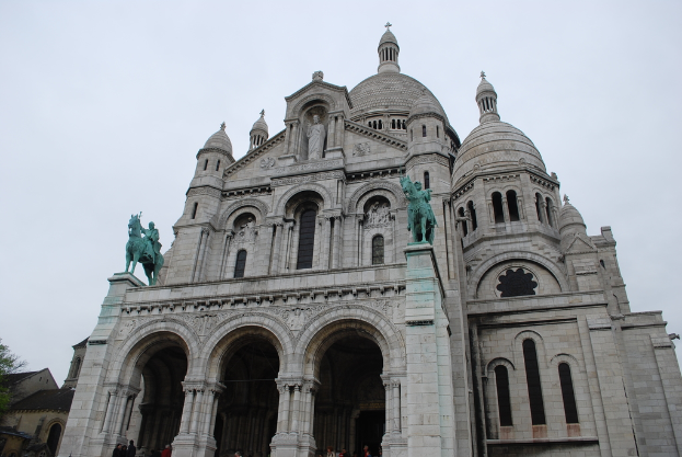 Ein Denkmal steht in der Bildmitte, mit Häusern und einem Baum in der unteren linken Ecke.