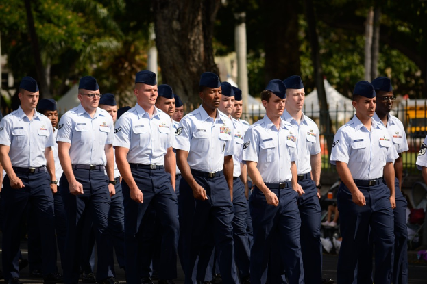 Mönner in Uniform auf einer Straße mit einem Eisengelönder im Hintergrund, Bürge und Masten im Hintergrund.