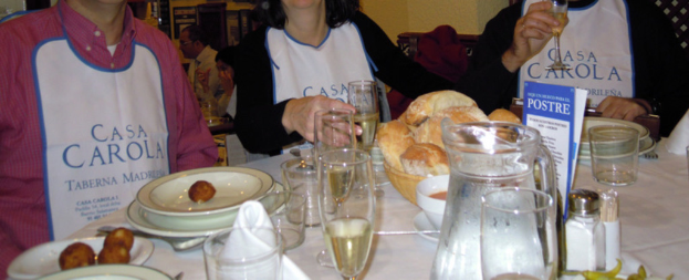 Menschen sitzen an Tischen mit Tellern, Besteck, Brotkörben, Gläsern und einer Werbung.