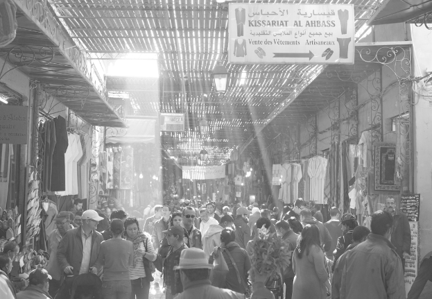 Ein Schwarz-Weiß-Bild einer Gruppe von Menschen, die auf einer Straße flanieren, die von Geschäften gesäumt ist, mit einem Schild über den Geschäften.