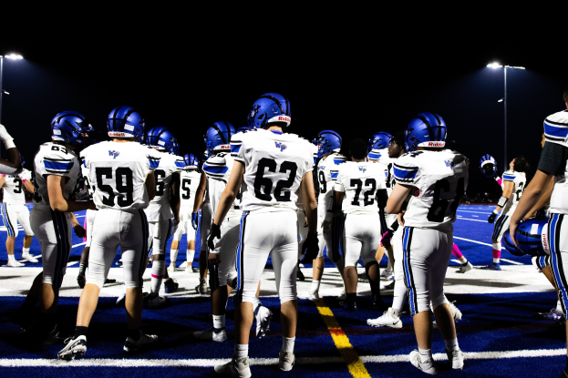 Eine Gruppe von Fussballspielern in Helmen und Stiefeln steht auf einem Feld, mit beleuchteten Lichtmasten im Hintergrund.