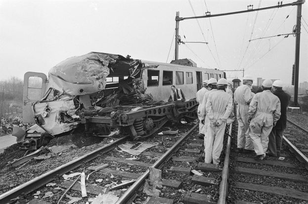 Ein Schwarz-Weiß-Bild einer Zugkollision auf den Schienen mit Einsatzkräften in Helmen und sichtbaren Infrastruktur.