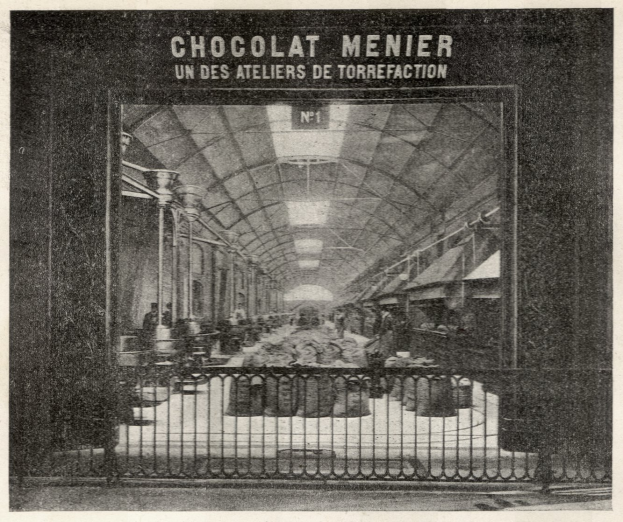 Ein altes Schwarz-Weiß-Foto eines Bahnhofs mit Menschen, Gittern, Pfählen, Lampen und einem Dach, mit dem Text "Chocolat Menier - Un des Ateliers de Torrefaction" oben.