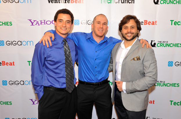 Drei Personen vor einer Sponsorentafel, bekleidet.