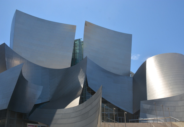Die ARTIST Concert Hall in Los Angeles, ein modernes Gebäude mit Glaswänden und Treppen mit Geländern, die zur Eingangstür führen, umgeben von Laternenmasten, mit einer Tafel mit Text im Vordergrund und einem bewölkten Himmel im Hintergrund.