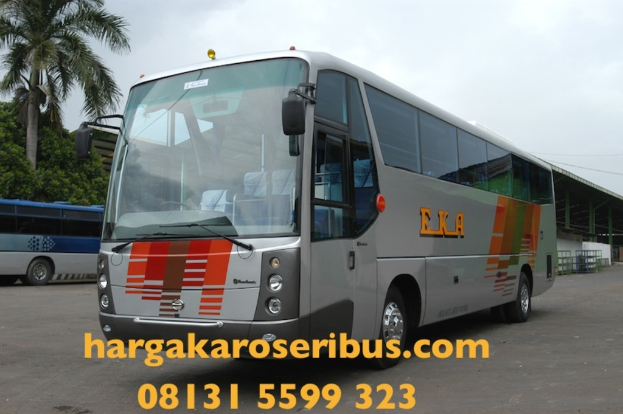 Ein grauer Bus in der Mitte, ein blauer Bus links, Bäume, ein Schuppen rechts, Himmel oben und Kontaktinformationen unten.