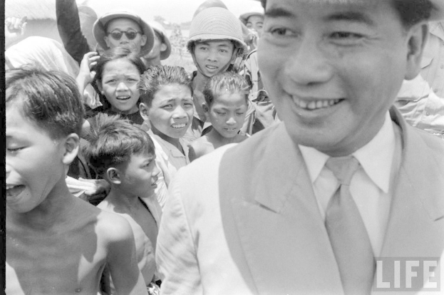 Ein Schwarz-Weiß-Bild von Kindern mit einer Person auf der rechten Seite, die Kleidung trägt und einen Text in der rechten unteren Ecke.