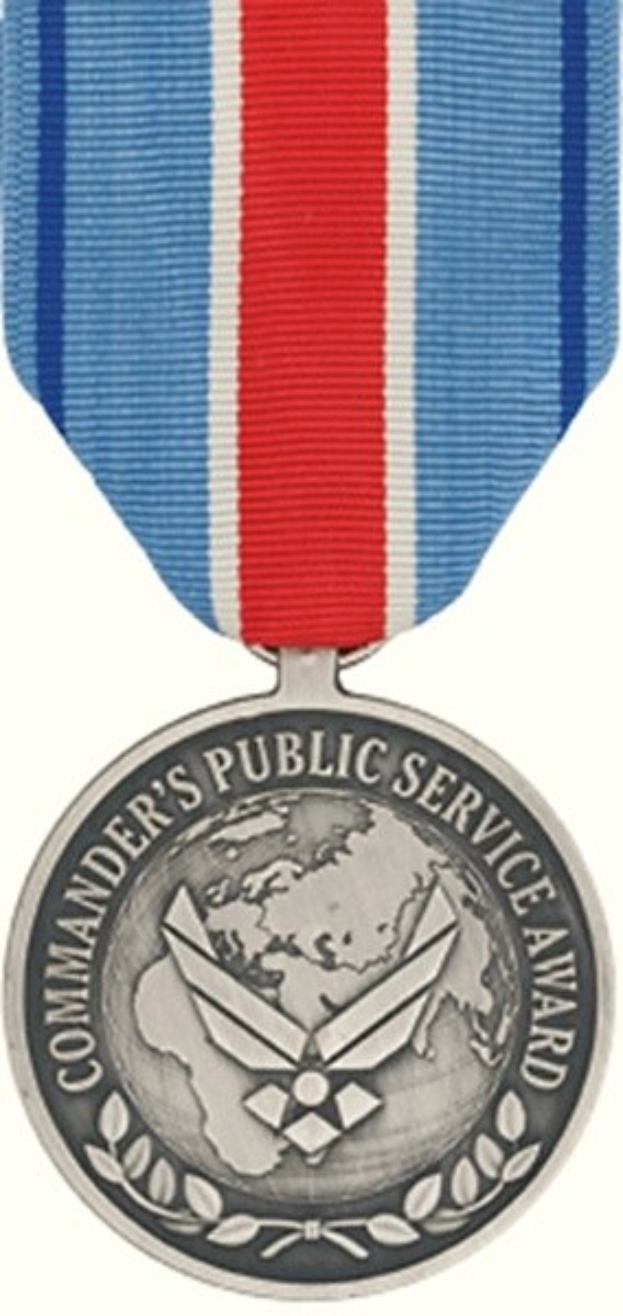 Silberne Medaille mit rot-weiß-blauem Band, beschriftet mit 'Commander's Public Service Award', vor weißem Hintergrund.