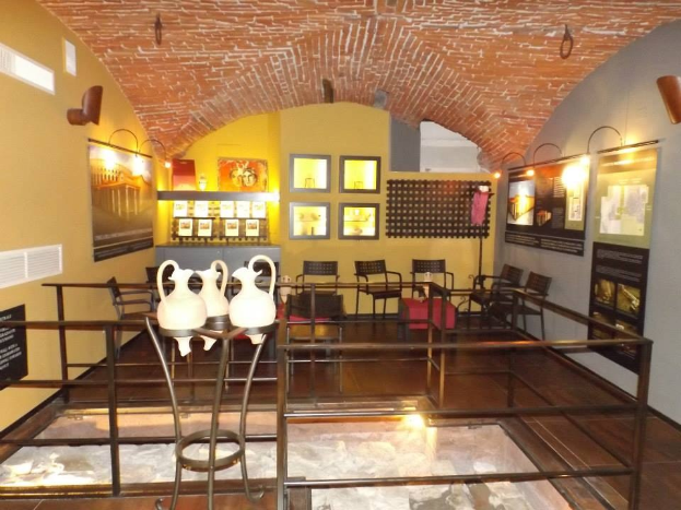 Ein geräumiger Museumsraum mit mehreren Tischen, Stühlen, Displaytafeln, gerahmten Kunstwerken an den Wänden, dekorativen Vasen, Leuchten und anderen Ausstellungsstücken.