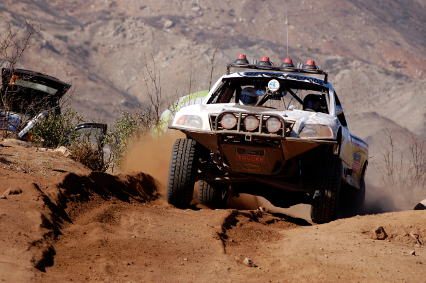 Ein weißes Auto fährt in der Mitte einer Straße mit grünen Pflanzen auf der linken Seite.
