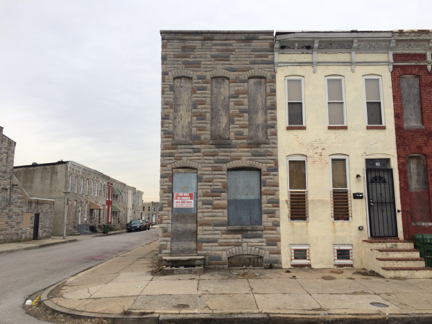 Ein altes, baufälliges Gebäude an einer Straßenecke mit kaputten Fenstern, bröckelnden Wänden, vorbeifahrenden Fahrzeugen, Mülltonnen am Gehweg und einem klaren blauen Himmel im Hintergrund.