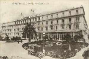 Eine schwarz-weiße Postkarte des Hotels Riviera-Palace in Nice-Cimiez mit einem Auto, Menschen und dem Gebäude mit Fenstern, Bäumen, Pflanzen, Laternen und Fahnen mit Stangen.
