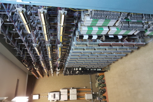 Ein geräumiger Raum voller numerous Wires und elektronischer Geräte auf dem Boden, mit einer Wand auf der linken Seite, ähnlich wie ein Datenzentrum mit verschiedenen Servern und miteinander verbundenen Kabeln.