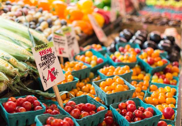 Ein Bauernmarkt mit Körben voller frischer Erzeugnisse, darunter Tomaten und Mais, mit Texttafeln im Hintergrund.