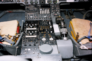 Ein Cockpit eines Flugzeugs mit einem Instrumentenbrett voller Knöpfe, Schalter und Tasten sowie einem Sitz in neutralem Stoff.