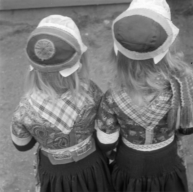 Zwei junge Maedchen in traditioneller bayerischer Tracht und Hauben stehen nebeneinander vor einer Wand, dargestellt in Schwarz-Weiss.