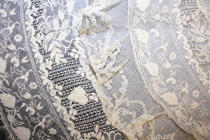 Nahaufnahme eines weißen Hochzeitskleids mit feiner Spitzenverzierung, das zarte und verschiedene Muster auf einem leichten, luftigen Stoff zeigt.