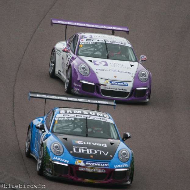 Zwei Autos fahren auf einer Straße außerhalb einer Stadt, mit Text in der unteren linken Ecke.