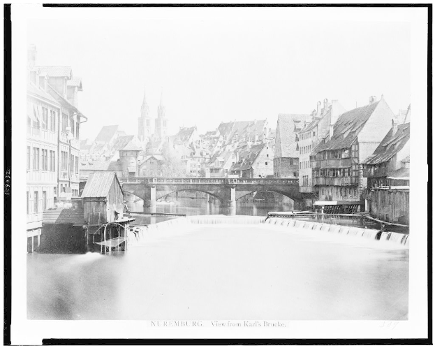 Ein Schwarz-Weiß-Foto eines Flusses mit einer Brücke darüber, umgeben von Gebäuden mit Fenstern, Bäumen und einem Himmel im Hintergrund, mit dem Text "Nürnberg, Blick von Karl's Brücke" unten.