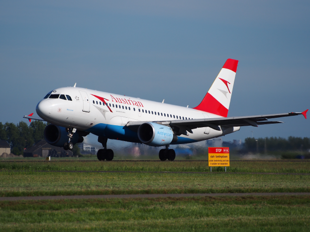 Ein Airbus A320-200 der Austrian Airlines startet am Frankfurter Flughafen, mit einem Schild im Vordergrund, Gras, Bäumen und Gebäuden im Hintergrund und einem klaren blauen Himmel.