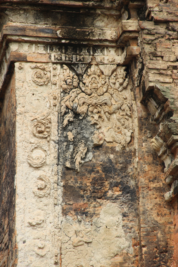 Ein altes Backsteingebäude mit einer detaillierten, kunstvollen Steinplastik auf der Seite, die verschiedene Formen und Symbole zeigt.